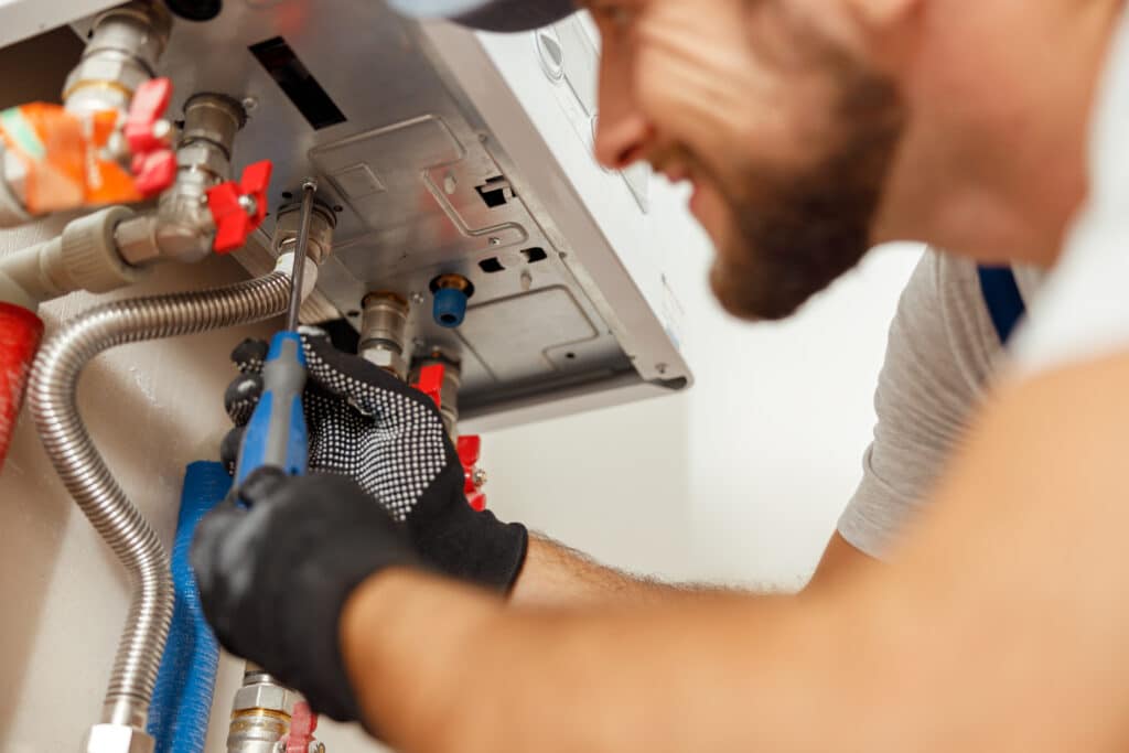 Closeup of plumber using screwdriver while installing new steel hot water central heating system in apartment. Manual work, maintenance, repair service concept